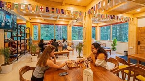 A wooden interior with large windows, a chess table, and a bookshelf. Flags are hanging from the ceiling. - The Hosteller Kasol (Bhuntar)
