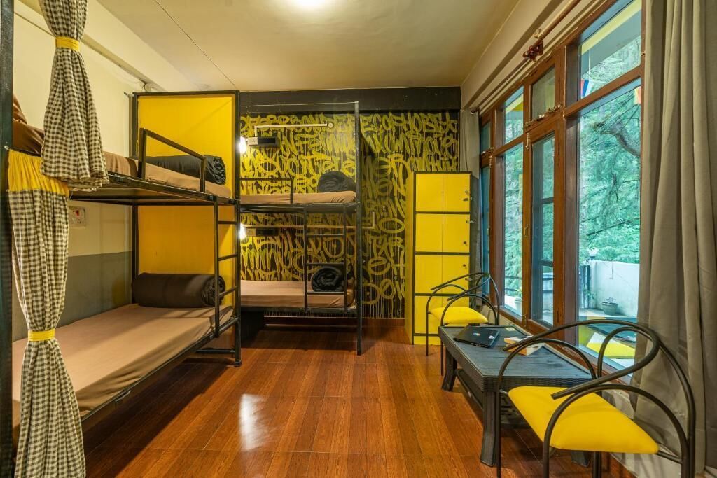 Una habitación tipo dormitorio con literas, una pequeña mesa con sillas y una ventana con cortinas.