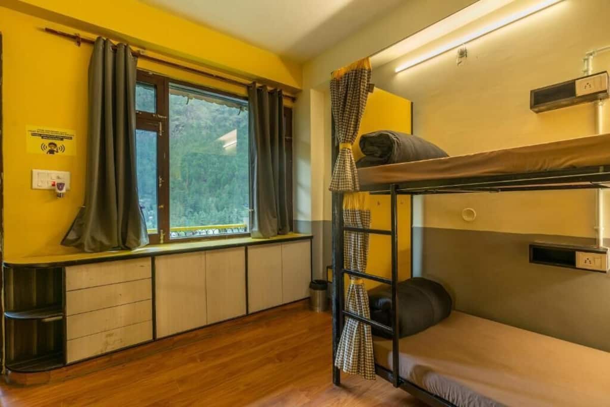 A bunk bed room with a window, curtains, a radiator, and a small shelf.