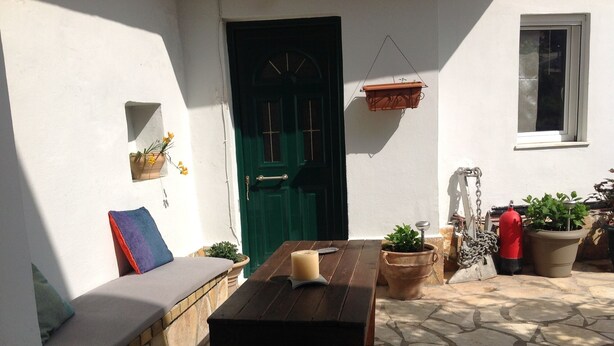 Eine Terrasse mit einem Holztisch, einer grünen Tür und Blumentöpfen.