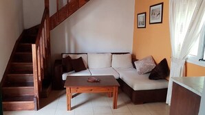 Ein Wohnzimmer mit einer Holztreppe, einem Sofa mit Kissen, einem Couchtisch und gerahmten Bildern an der Wand.