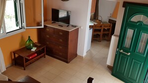 Ein Zimmer mit einem Holzkoffer, einem Fernseher darauf, einem Esstisch mit Stühlen und einer grünen Tür.