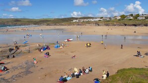 Ein weiter Sandstrand mit Menschen, die spazieren gehen und sitzen, Zelten und einigen Häusern im Hintergrund.