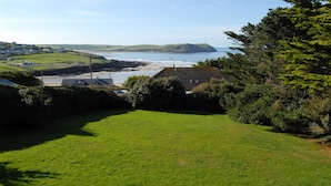 Eine Küstenlandschaft mit einer grasbewachsenen Vordergrundfläche, einem Strand und Blick auf das Meer sowie entfernte Hügel.