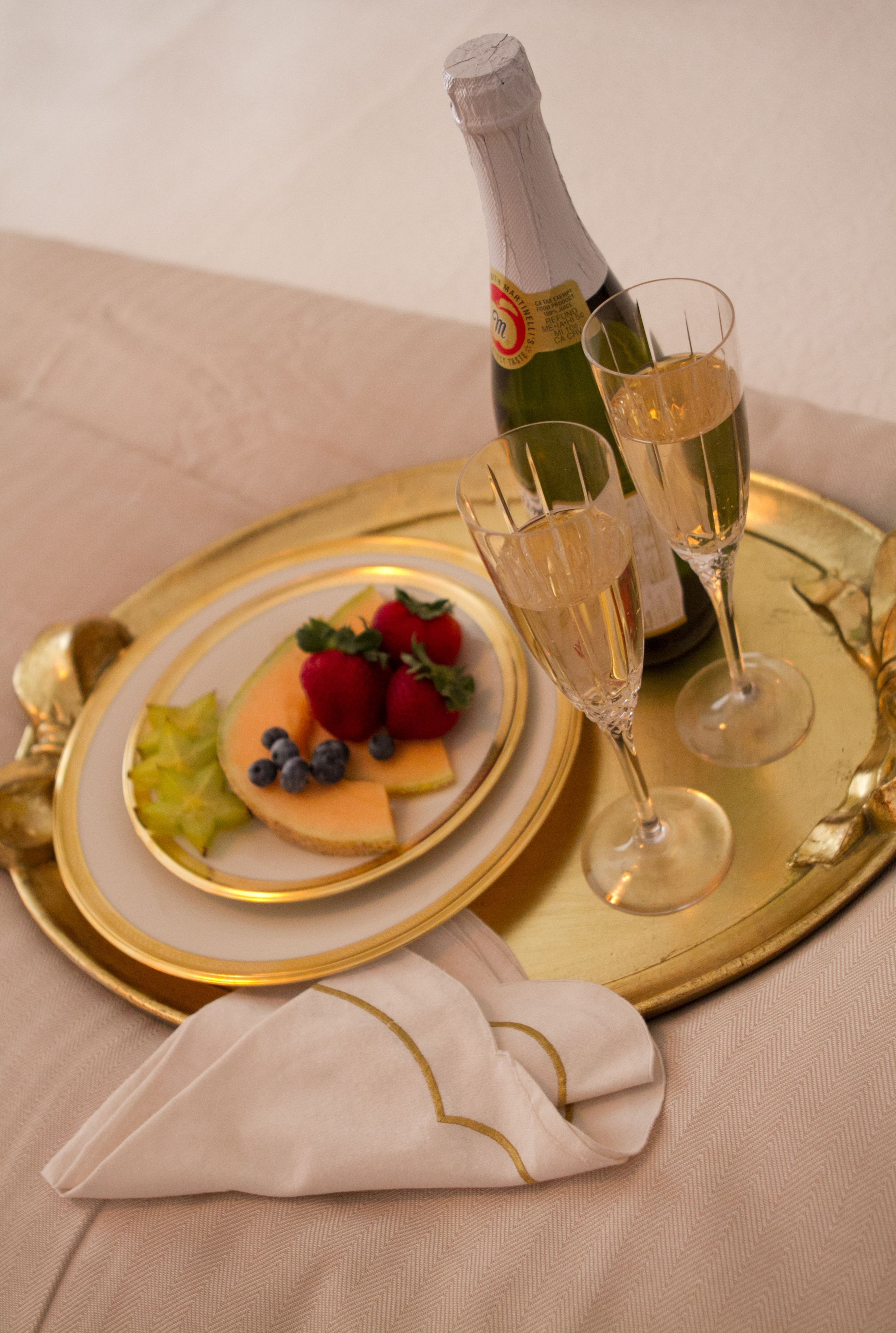 A champagne bottle, two glasses, and a plate with fruit on a gold tray.