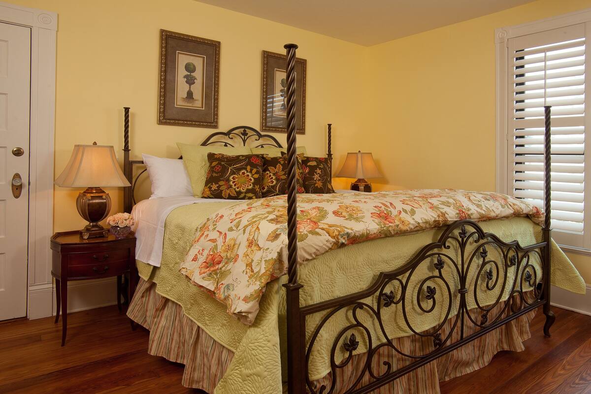 A neatly arranged bedroom with a four-poster bed, two bedside tables with lamps, and framed pictures on the wall.