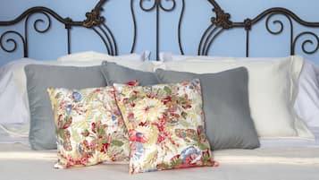 Una cama con cabecera de metal, dos almohadas florales y una colcha blanca.