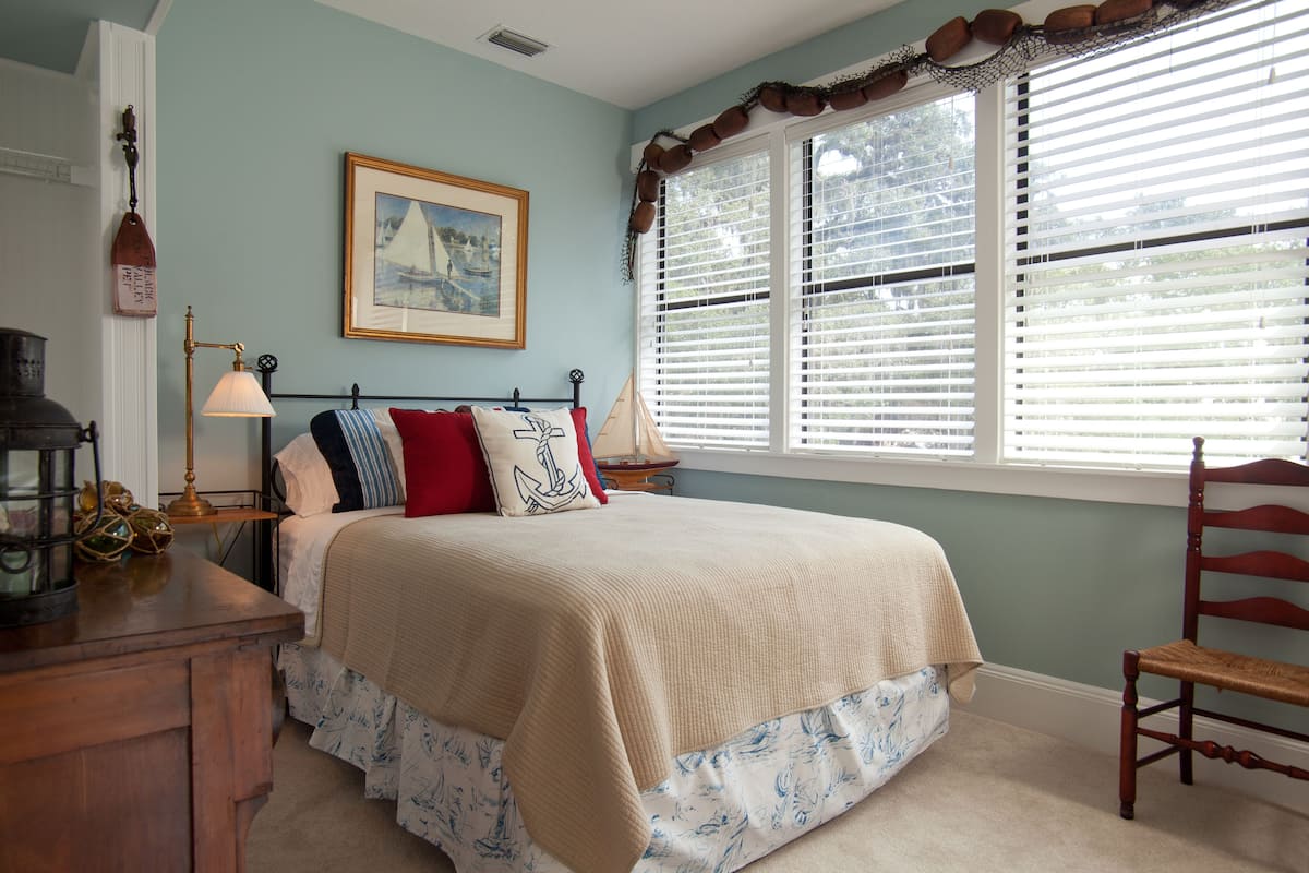 A bedroom with a bed, a nightstand, a lamp, a chair, and a window with blinds.