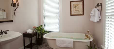 Un baño con una bañera tipo pata de león, un lavamanos y un espejo. Hay un cuadro en la pared y una planta en maceta en el suelo.