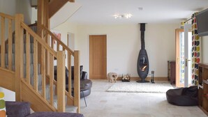 A living room with a wooden staircase, a fireplace, a sofa, and a dog.
