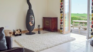 A living room with a wood-burning stove, a sofa, a rug, a cabinet, and a view of a garden through a glass door.