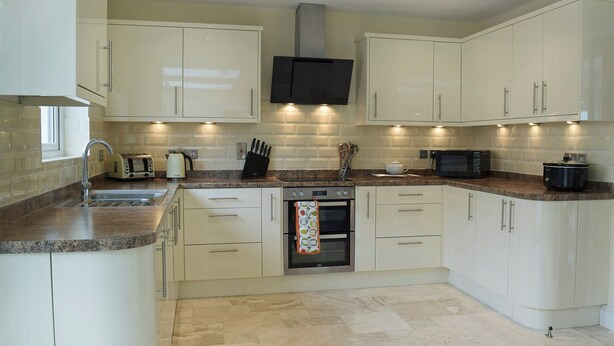 A modern kitchen with white cabinets, granite countertops, a built-in oven, and a stainless steel sink.