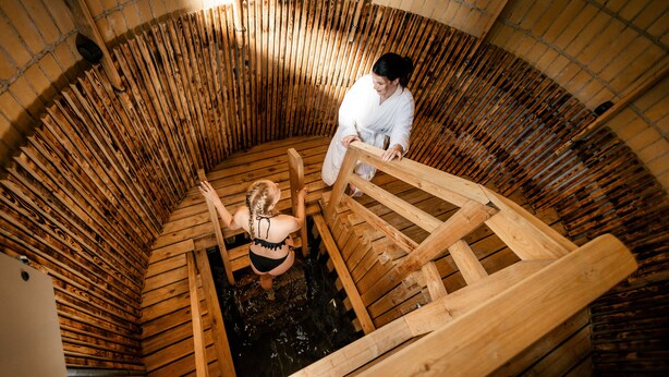 Ein traditionelles hölzernes Badehaus mit einer runden Holzkonstruktion, darin steht eine Person.