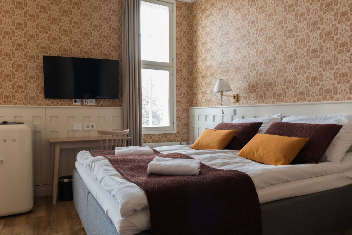 Una habitación de hotel con una cama, un televisor montado en la pared, un escritorio y una lámpara.