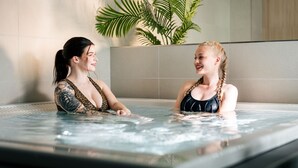 Zwei Frauen in einer Whirlpool-Badewanne, im Hintergrund eine Pflanze.