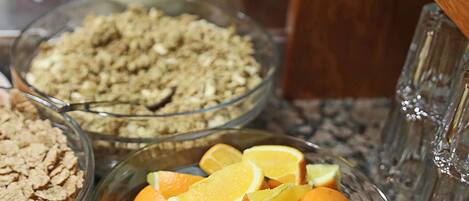 A buffet table with various food items including bowls of cereal, orange slices, and milk.