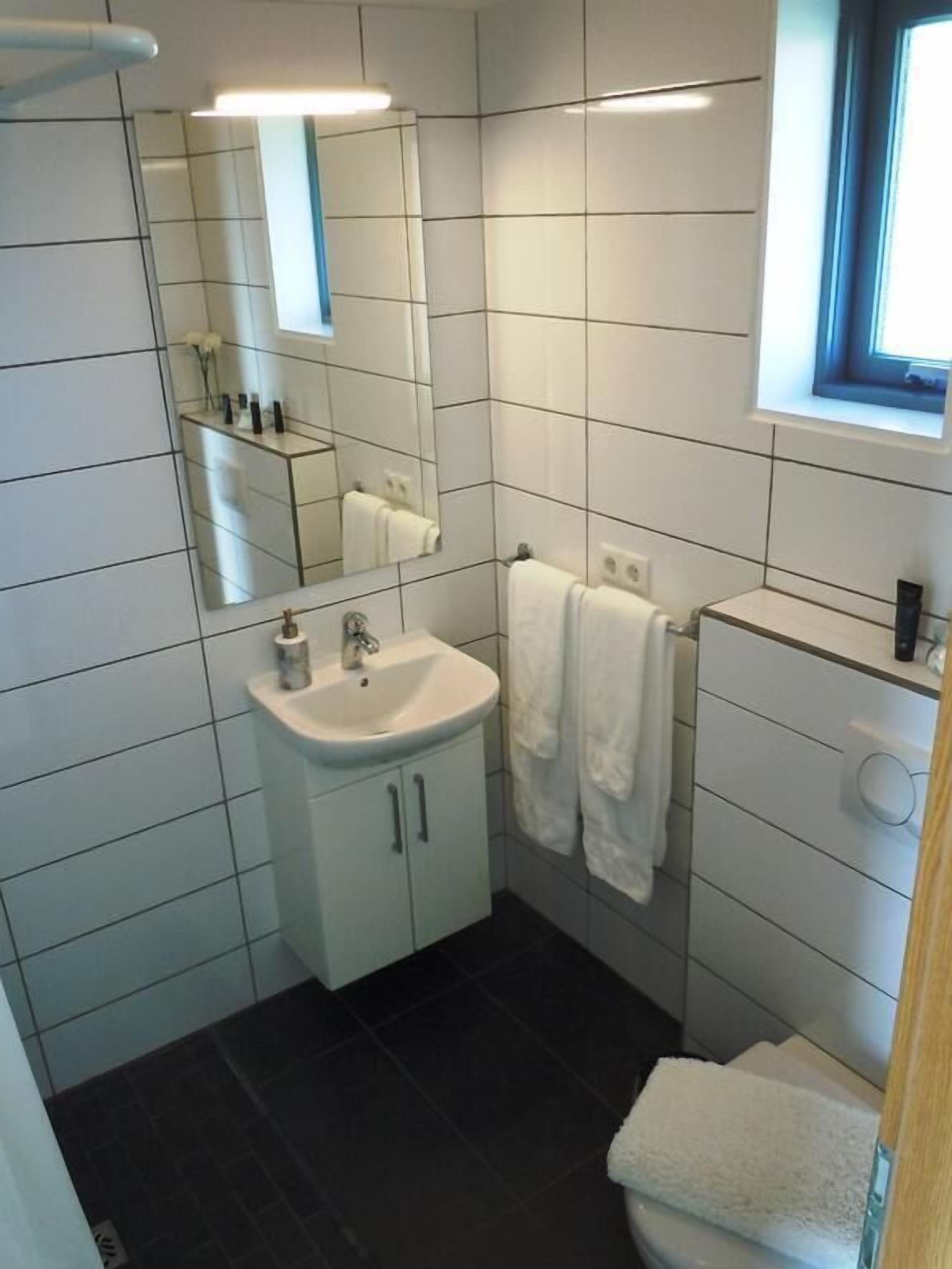 Un baño pequeño y moderno con azulejos blancos, un lavabo con tapa de vidrio, un espejo y una ventana.