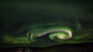 Una casa con porche visible y una estructura anexa, posiblemente un garaje o cobertizo, bajo un cielo nocturno con auroras boreales.
