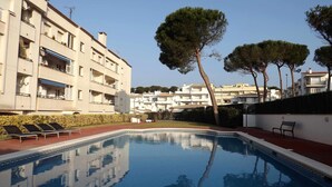 Une piscine avec des chaises longues, un bâtiment doté de balcons et des arbres en arrière-plan.