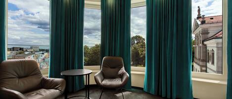 A room with two leather chairs, a small round table, and large windows with teal curtains.