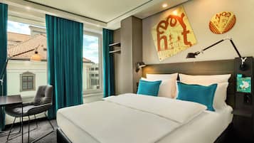Habitación de hotel con una cama grande, un escritorio y una silla. Hay una ventana con cortinas, una lámpara de pared y un cartel en la pared.