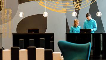 Un área de recepción con dos recepcionistas detrás de un mostrador, diseño de interiores moderno con arte abstracto en las paredes y una sala de espera con sillas coloridas.