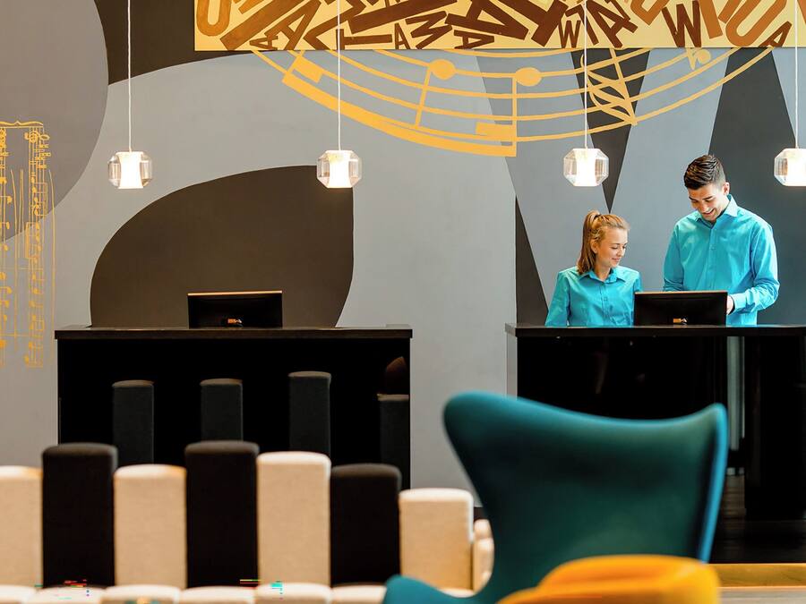 Un área de recepción con dos recepcionistas detrás de un mostrador, diseño de interiores moderno con arte abstracto en las paredes y una sala de espera con sillas coloridas.