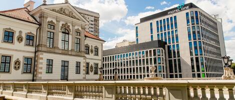 Un edificio histórico con arquitectura clásica y un edificio moderno con un letrero 'Motel One'.