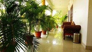 A corridor with potted plants, a patterned sofa, and a trash can. - Thayamkery's Royal inn (Kanayannur)