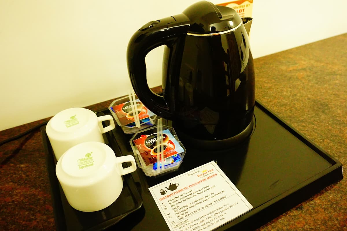 Una cafetera, dos tazas blancas y una bandeja con una bolsita de té e instrucciones sobre la mesa de una habitación de hotel.