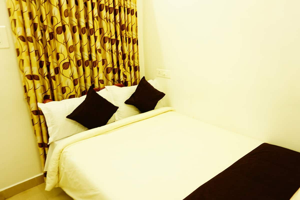 Una cama con ropa blanca y dos almohadas oscuras, una cortina estampada y una pared blanca.
