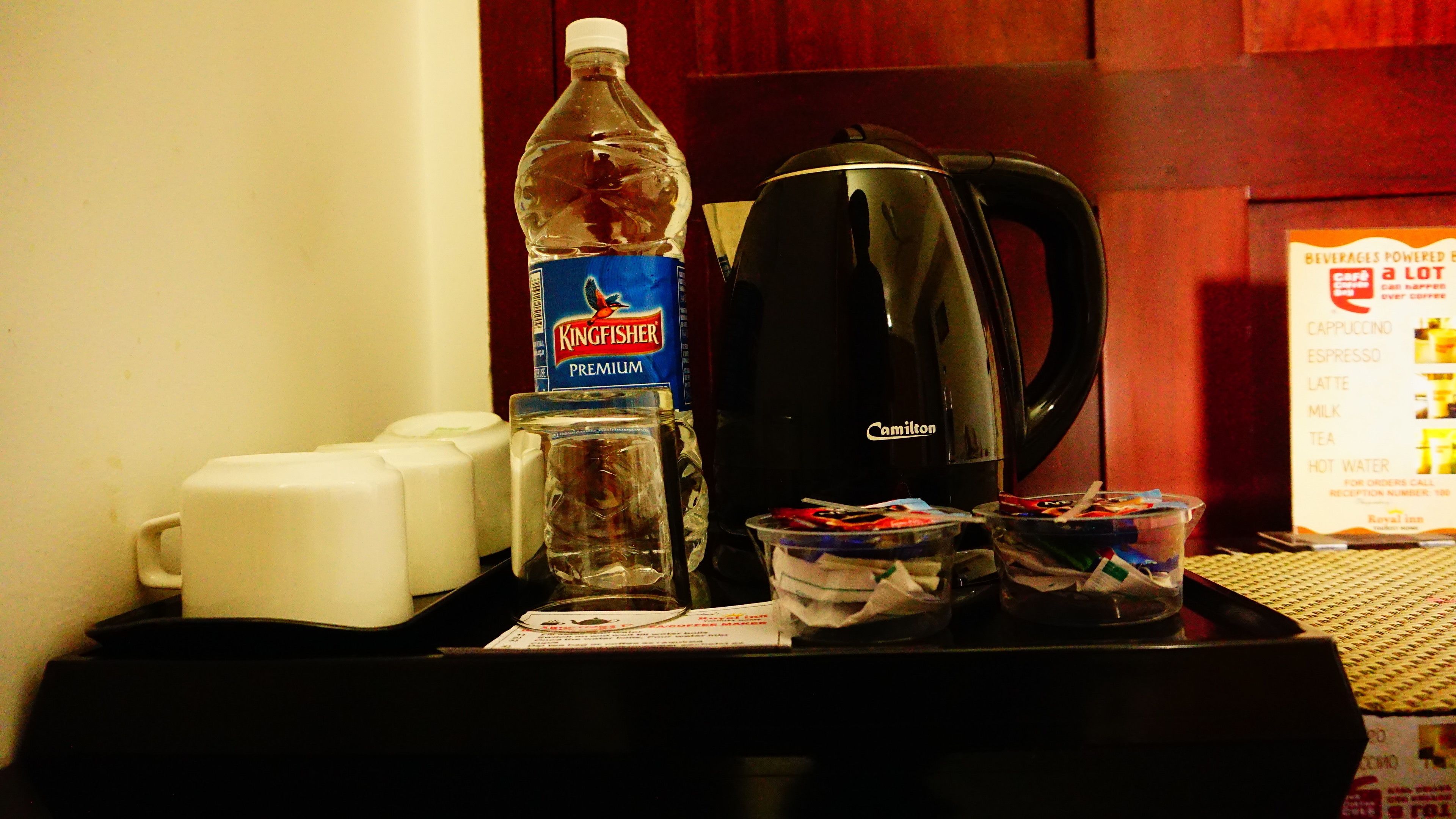 Un plateau de petit-déjeuner dans une chambre d’hôtel, avec une bouteille d’eau, une machine à café et une tasse de café.