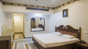 A hotel room with a bed, a bedside table, a mirror, a television, and a door leading to another room. - Hotel Shiraaz 1 (Panchkula)