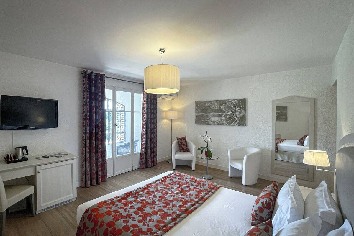 A hotel room with a bed, desk, chair, TV, and a window with curtains.