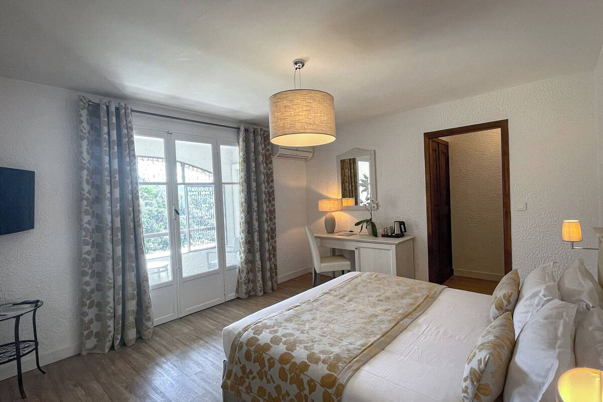A hotel room with a bed, a desk, a chair, a TV, and a door leading to a balcony.