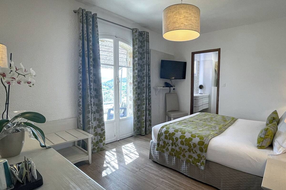 A hotel room with a bed, bedside lamps, a TV, a small table, and a window with curtains.