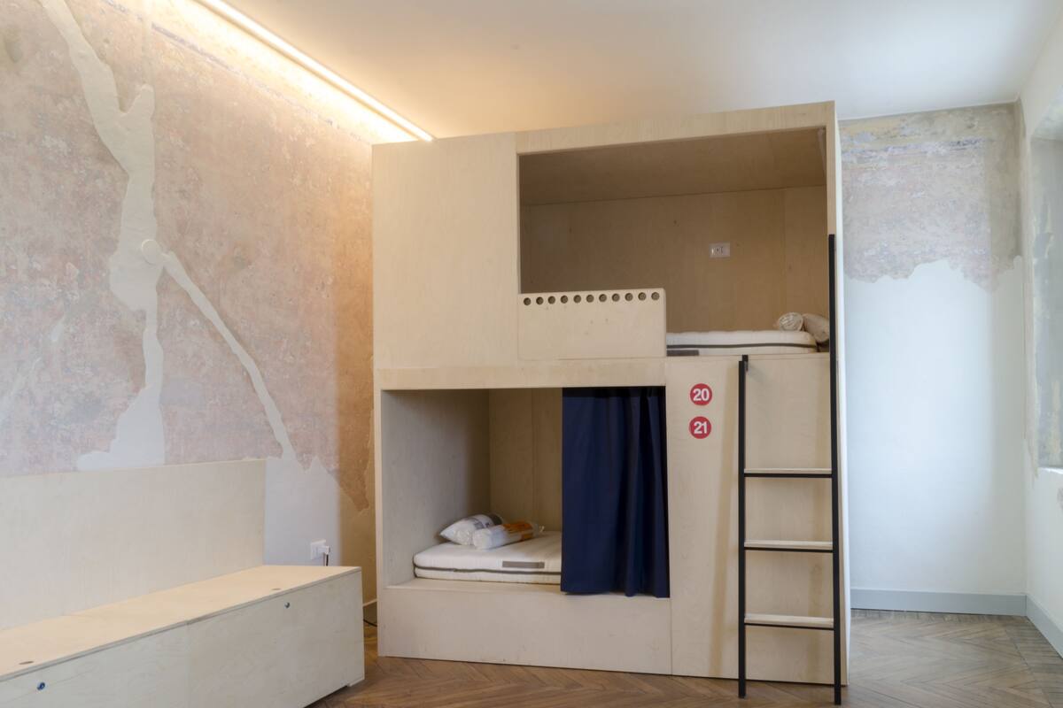 A bunk bed room with a ladder, a mattress, and a blue curtain.