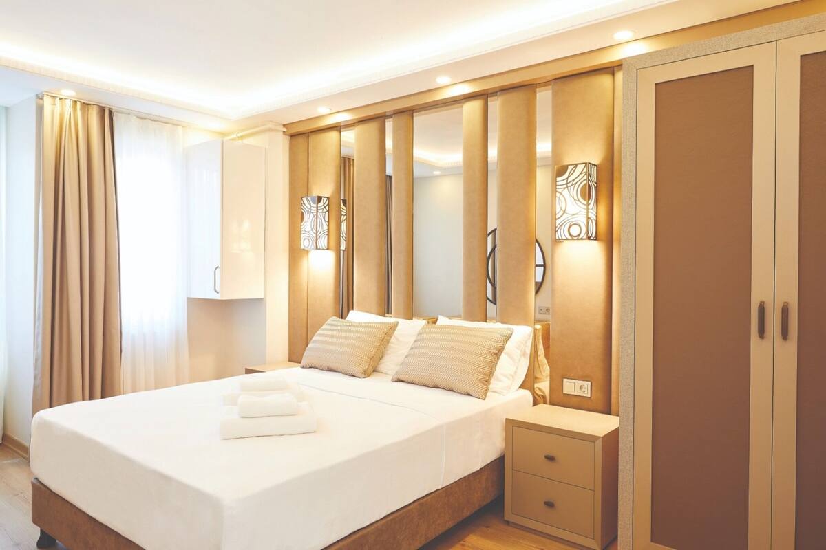 A hotel room with a large bed, bedside tables, a wardrobe, and decorative wall sconces.