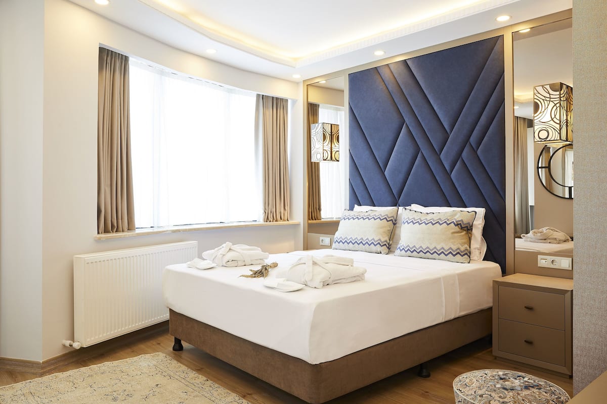 A modern hotel room with a large bed, bedside tables, a mirror, and a radiator.
