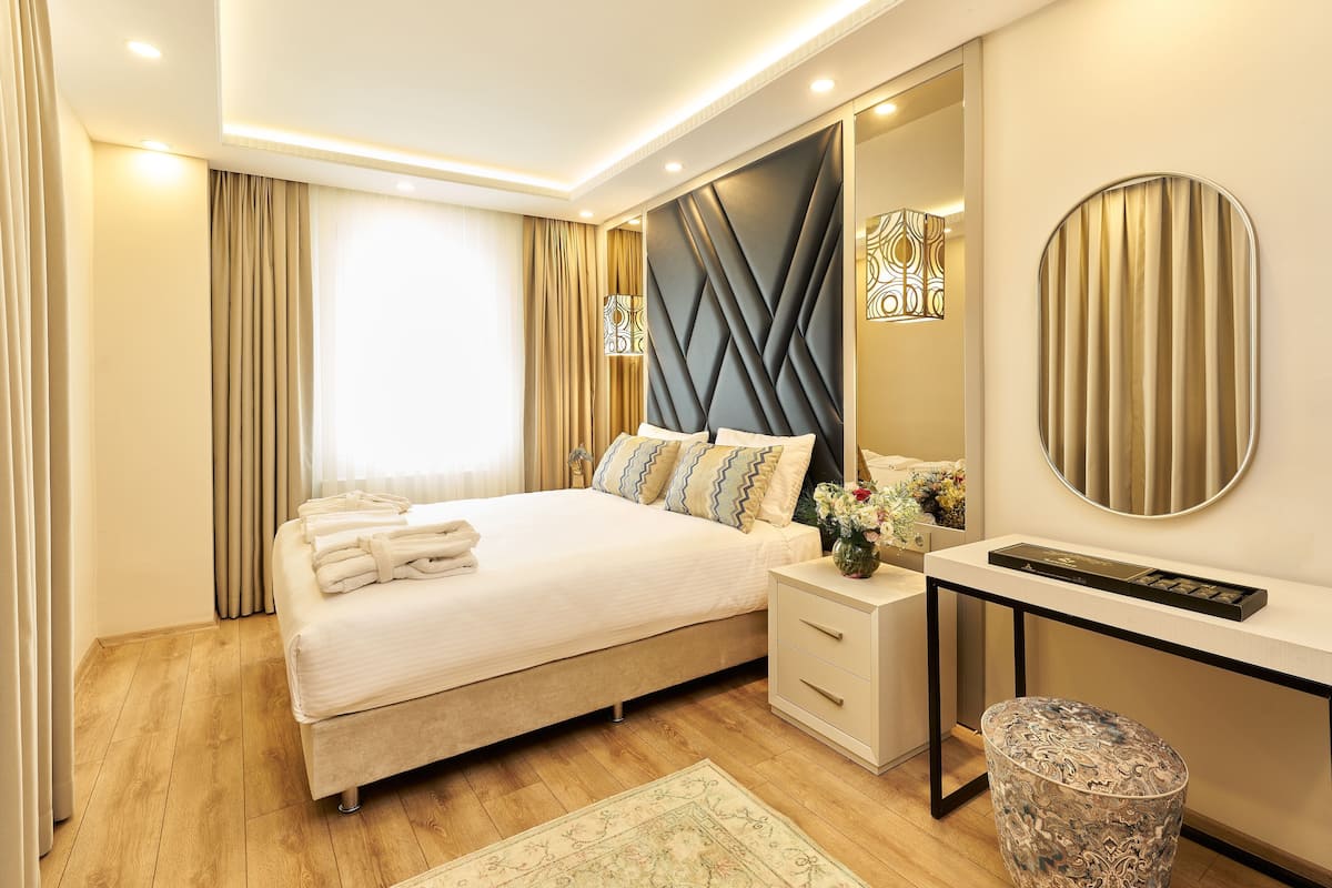 A modern hotel bedroom with a bed, bedside table, and a mirror.
