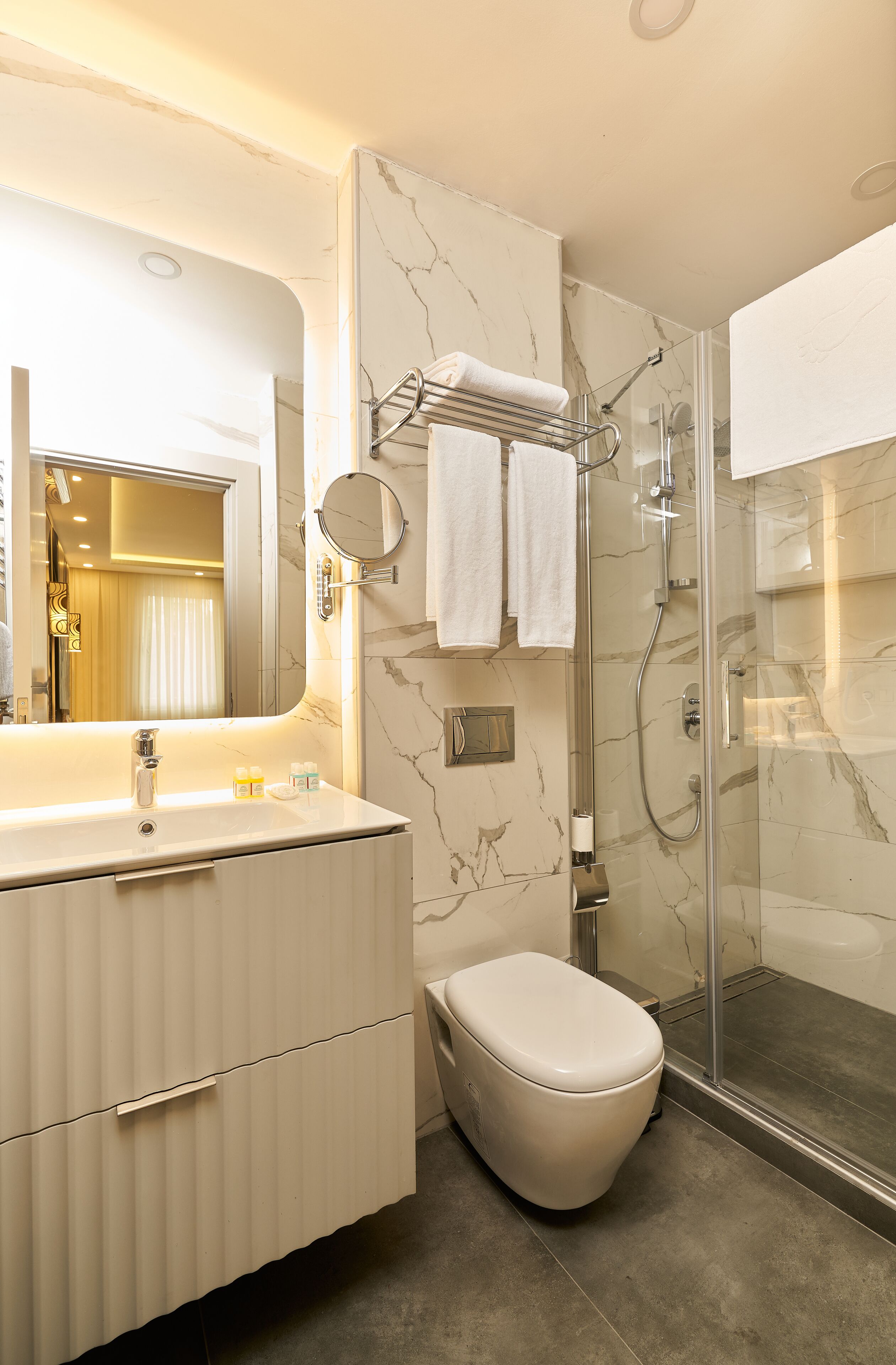 A modern bathroom with a marble vanity, a glass-enclosed shower, and a toilet.