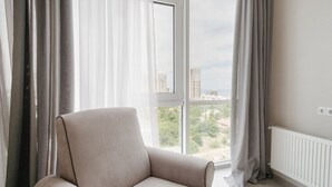 Moderni huone, jossa on suuri ikkuna, vaaleanbeige nojatuoli ja valkoinen patteri.