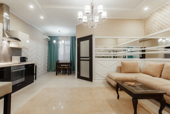 A modern living room with a sofa, coffee table, and dining area. There is a kitchen with a microwave and oven.