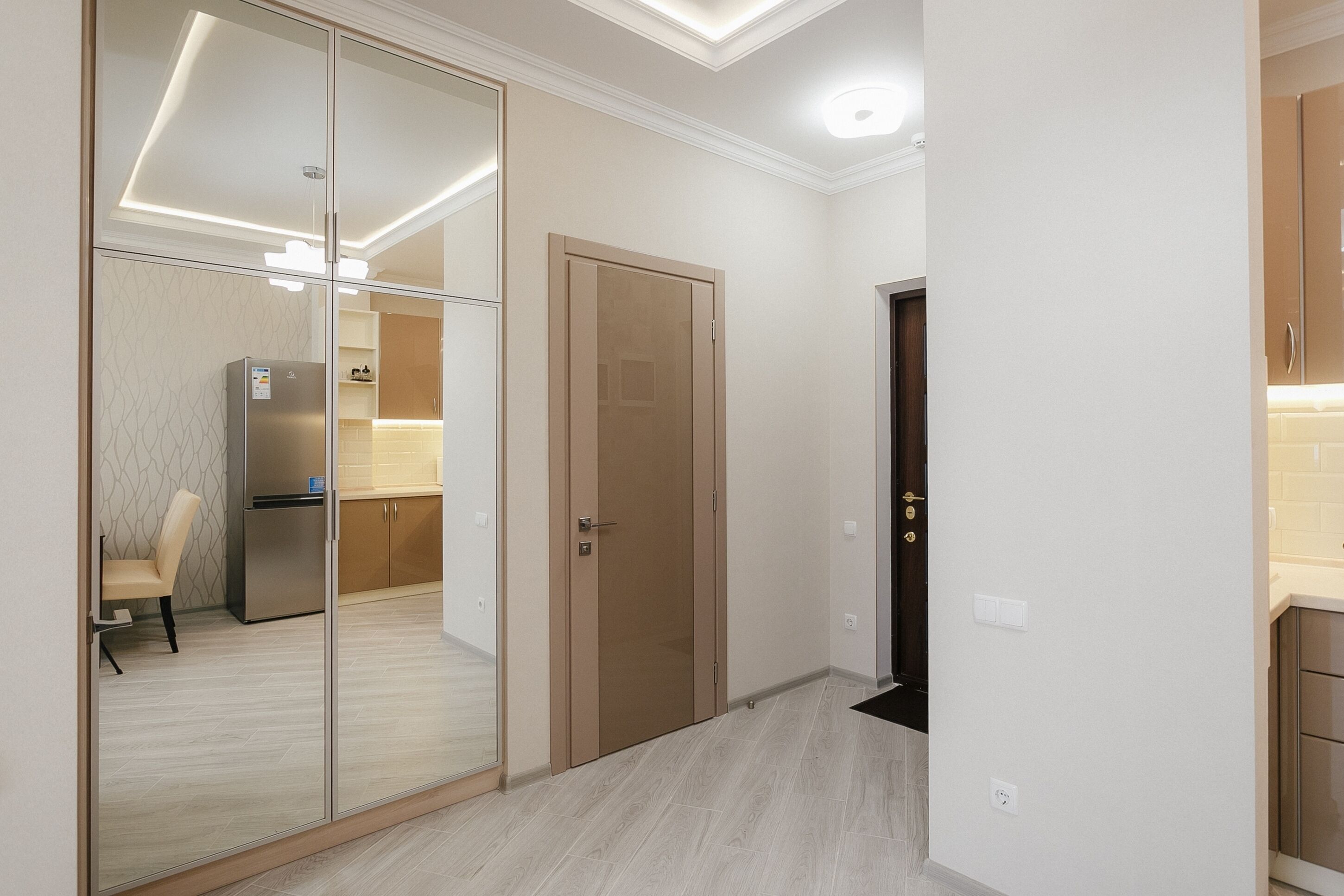 A modern kitchen with a refrigerator, a wooden door, and a light switch on the wall.
