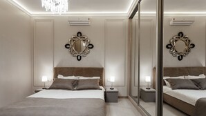 Moderni hotellihuone, jossa on suuri sänky, yöpöydät lampuineen, koristeelliset peilit ja sisäänrakennettu ilmastointilaite.