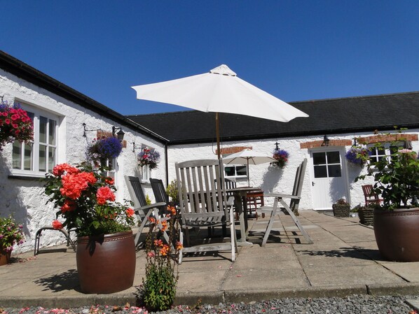 A white building with a black roof, outdoor seating with a white umbrella, and potted plants with flowers. - East Trewent Farm B&B (Pembroke)