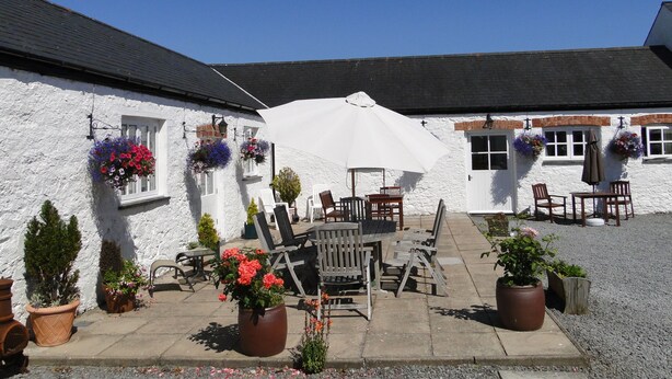 A white building with a patio area featuring outdoor seating and potted plants. - East Trewent Farm B&B (Pembroke)