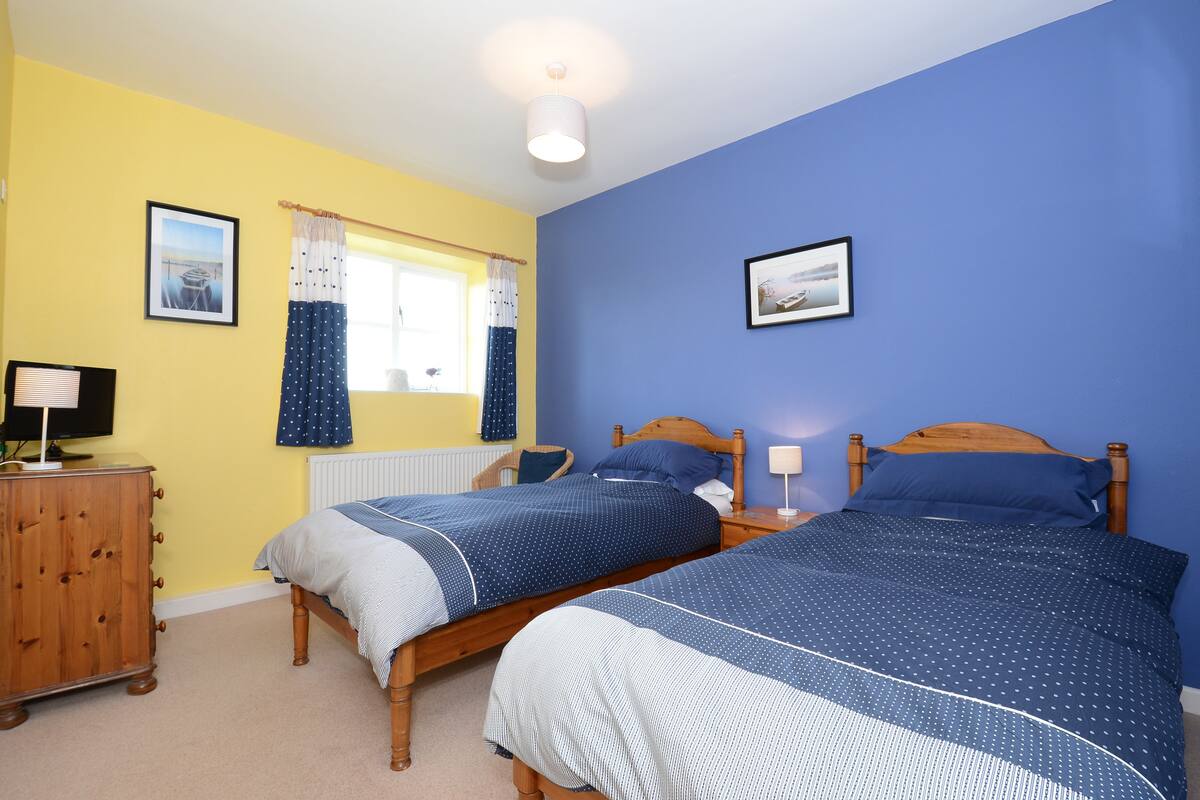 A bedroom with two single beds, a wooden dresser, a chair, and a window with curtains.