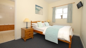 A bedroom with a bed, bedside lamps, a wooden nightstand, a window with curtains, and a wall-mounted TV. - East Trewent Farm B&B (Pembroke)
