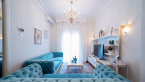 A living room with a blue sofa, a white coffee table, and a chandelier. - Acropolis Deluxe Apt Must (Thessaloniki)